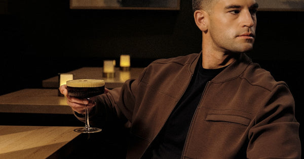 A man sitting alone in a candlelit room holding a coffee, considering it