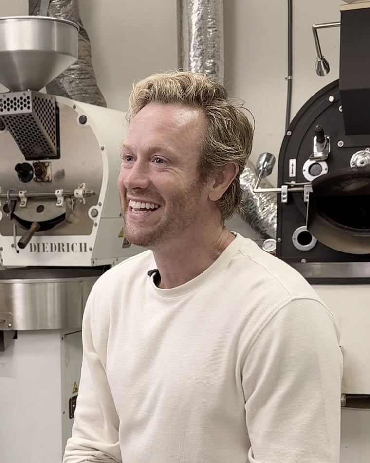 Jarrett Johnson smiling in a coffee roastery beside commercial coffee roasters